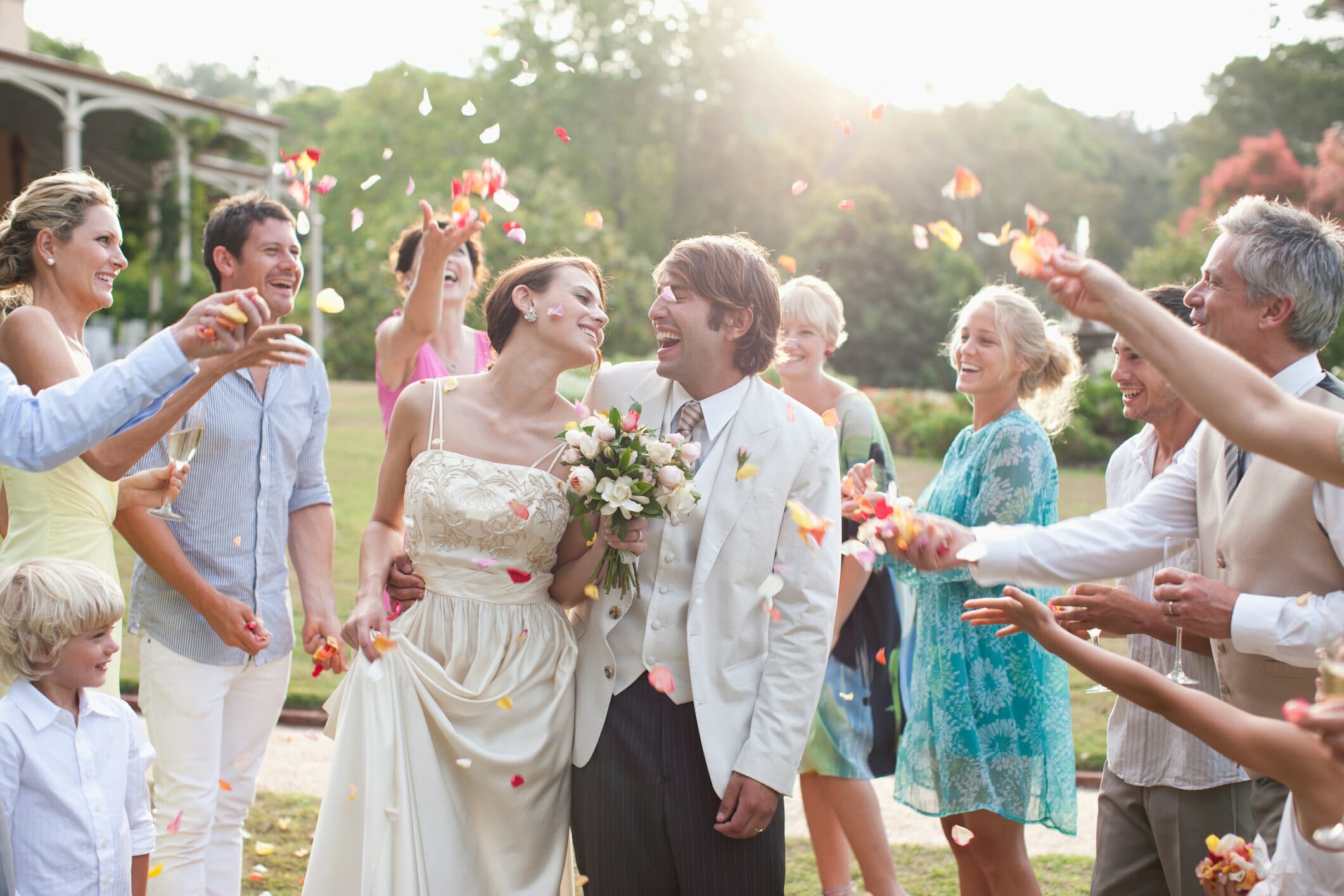 just married couple smile at each other as friends and family toss flower petals around them at their low budget wedding