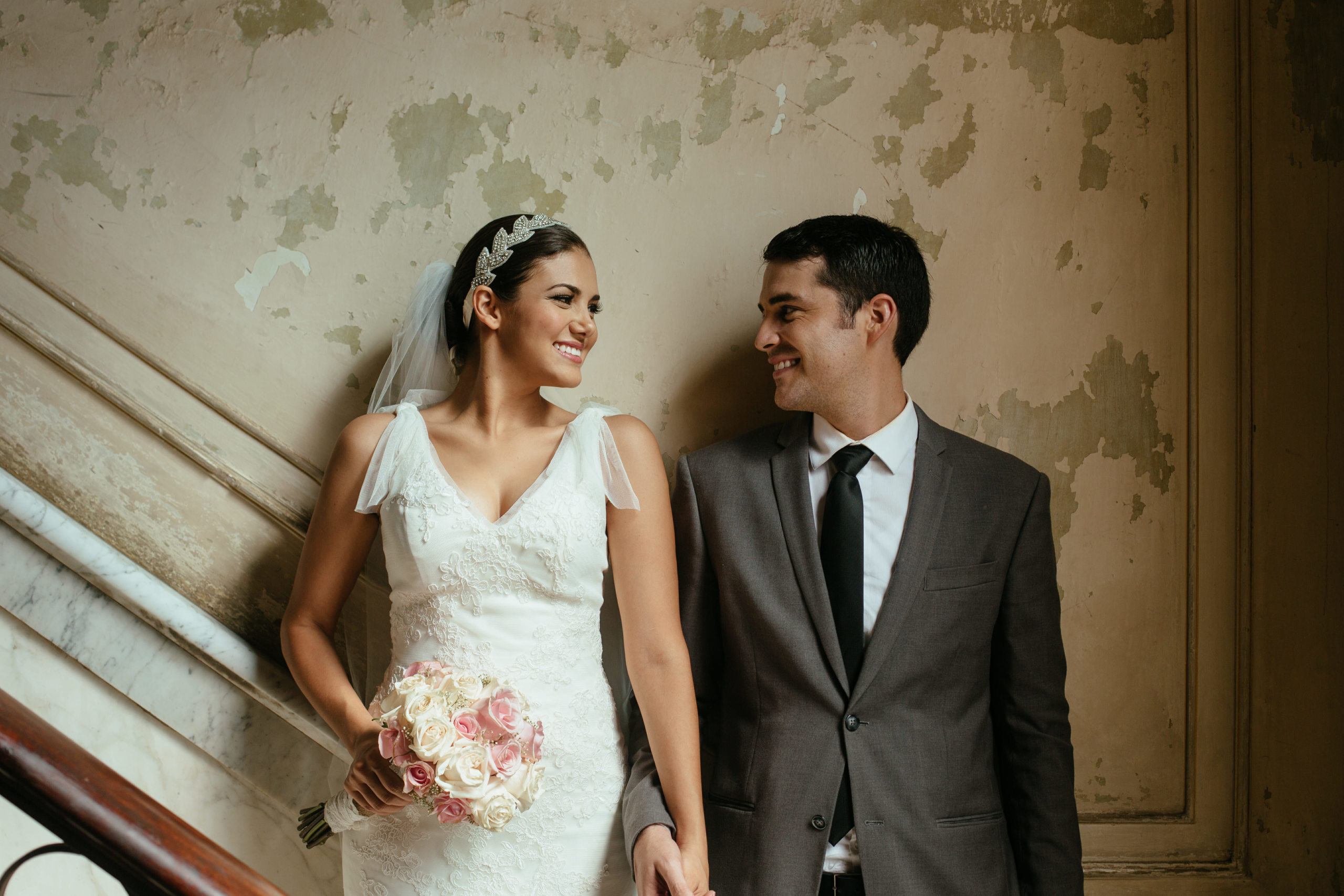 A newlywed couple holding hands while standing against the grunge wall in this horizontal shot. Havana Cuba.