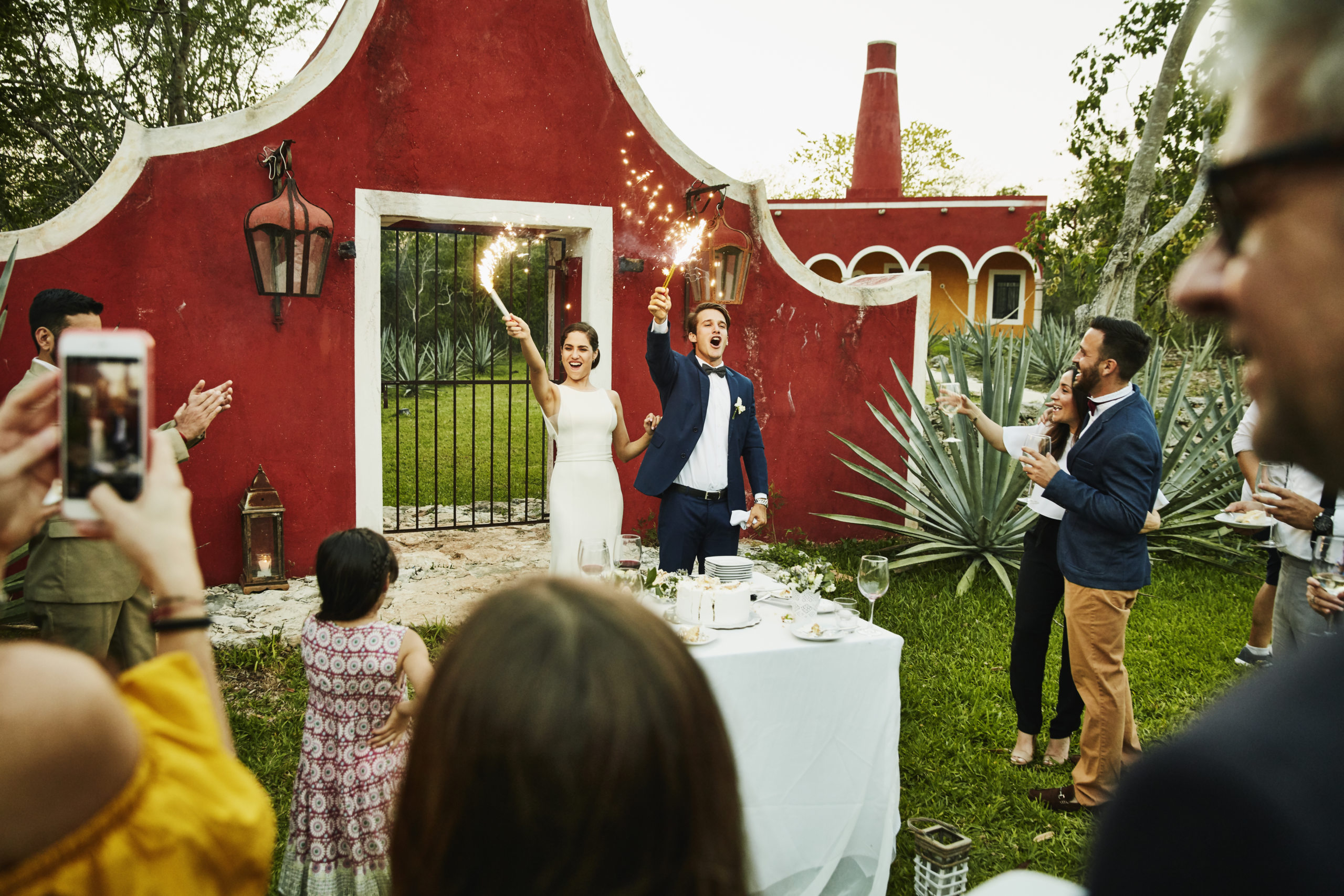 Bride and groom celebrating with sparklers after cutting cake during outdoor wedding reception