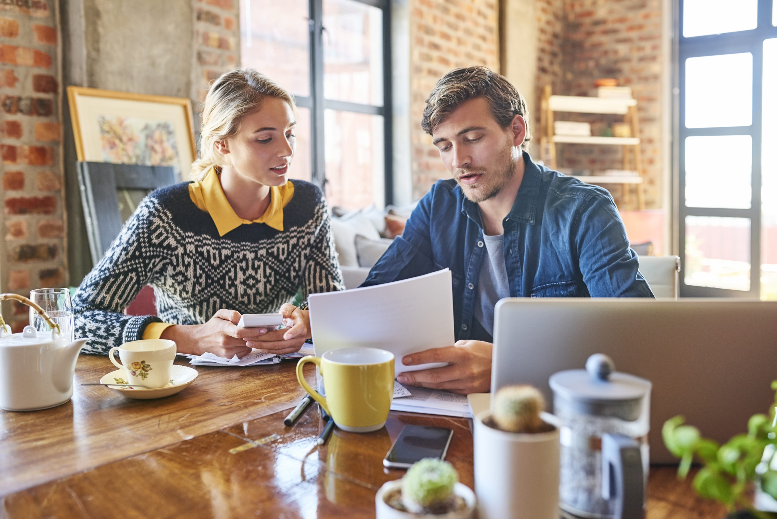 Young man and woman calculating home finance. Male and female partners are doing paperwork at table. They are wearing casuals at home.