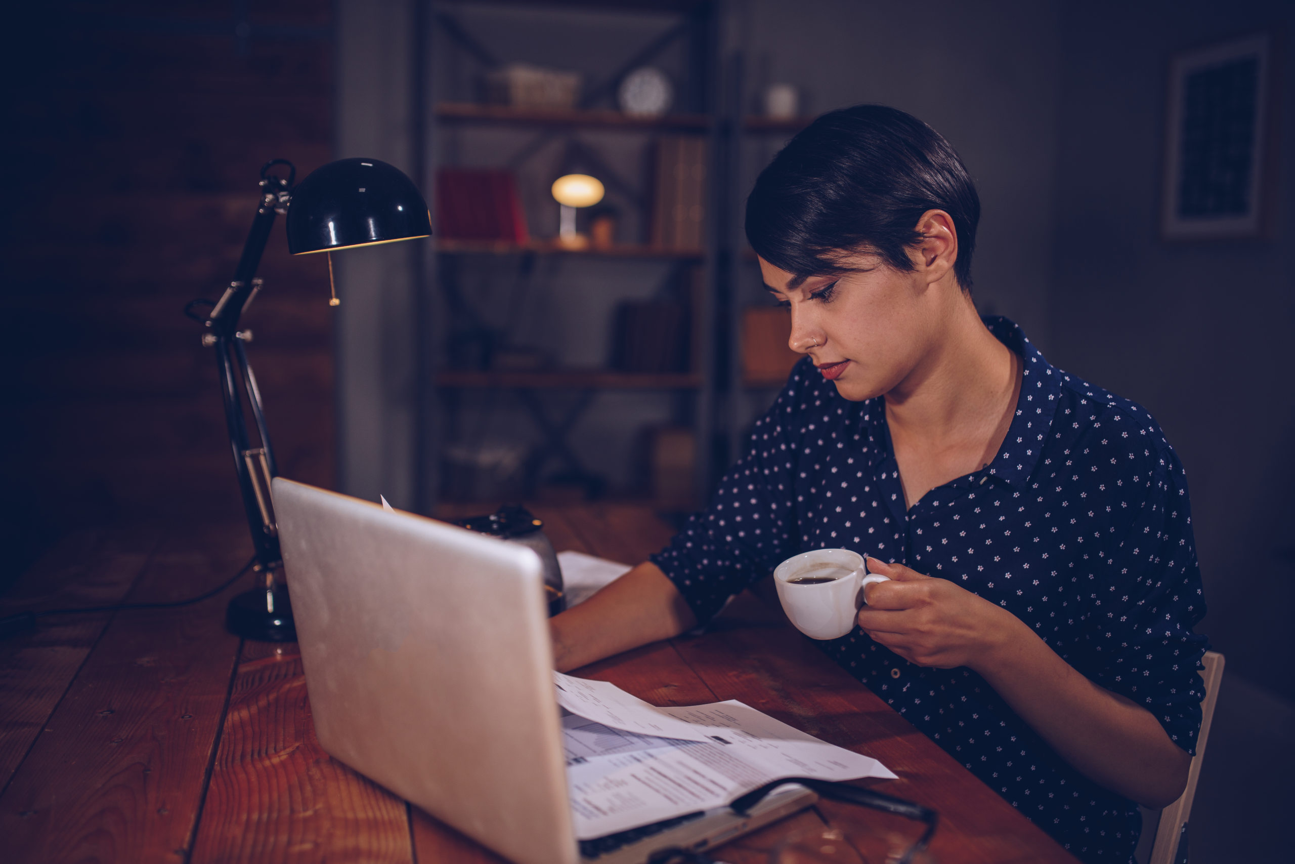 Young woman sitting at the table with laptop in front of her and looking at her laptop trying to figure out how to pay her student loans